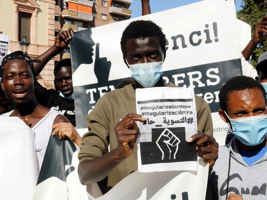 A man in Lleida holds up a sign calling for the regularization of undocumented migrants (by Anna Berga)